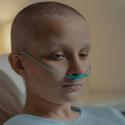 Porträt einer kahlköpfigen Person mit Nasenkanüle als Symbol für die psychische Belastung durch eine schwere Erkrankung.